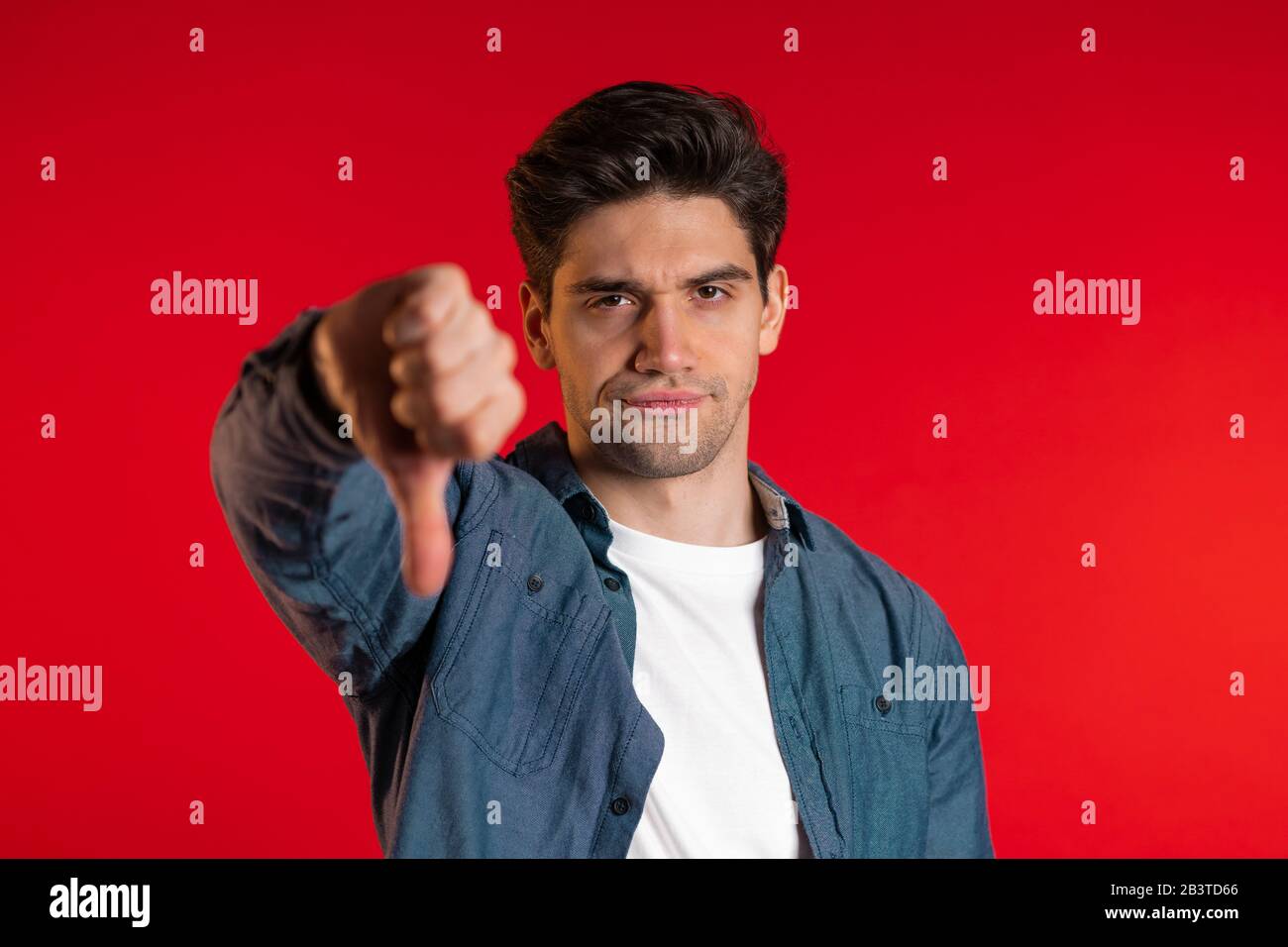 Giovane bell'uomo in piedi su sfondo rosso studio che esprime malcontento Foto Stock