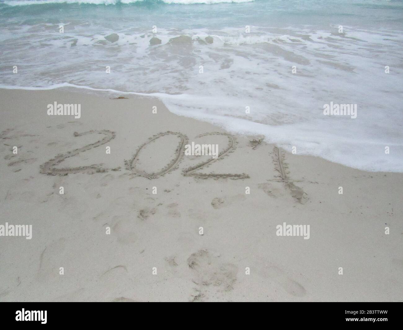 Felice anno nuovo 2021, scritta sulla spiaggia con onda e mare blu chiaro. Numeri 2021 anno sulla riva del mare, messaggio scritto a mano nella sabbia dorata Foto Stock