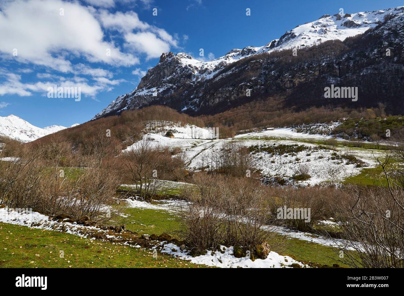 Teito, tradizionale dimora in pietra con tetto di paglia, e montagne innevate sullo sfondo (Valle del Lago, Parco Naturale Somiedo, Asturie, Spagna) Foto Stock