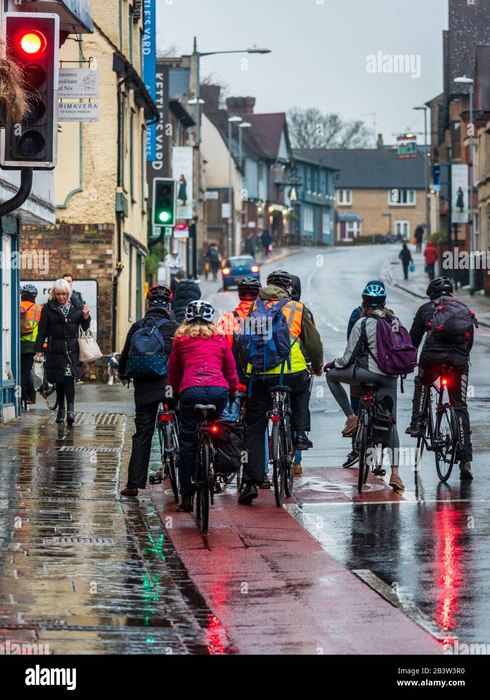 Pendolari in bicicletta sotto la pioggia. I Pendolari in bicicletta si trovano in coda al semaforo a Cambridge in prima serata. Ciclisti nella pioggia. Foto Stock