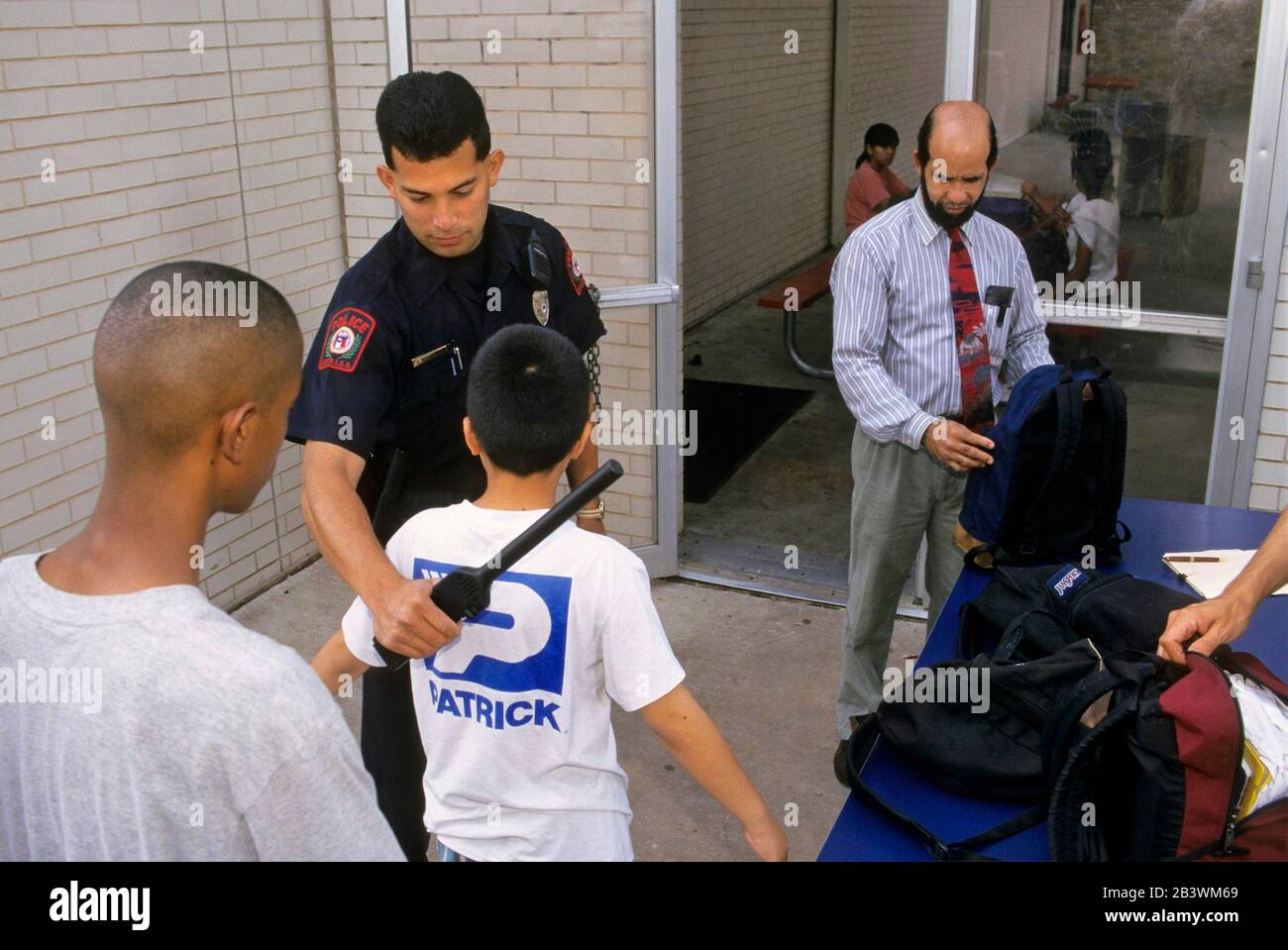 Austin Texas USA, circa 1997: Un ufficiale di polizia della scuola utilizza un metal detector mentre un insegnante ispeziona gli zaini quando gli studenti entrano nella scuola media all'inizio della giornata scolastica. ©Bob Daemmrich Foto Stock