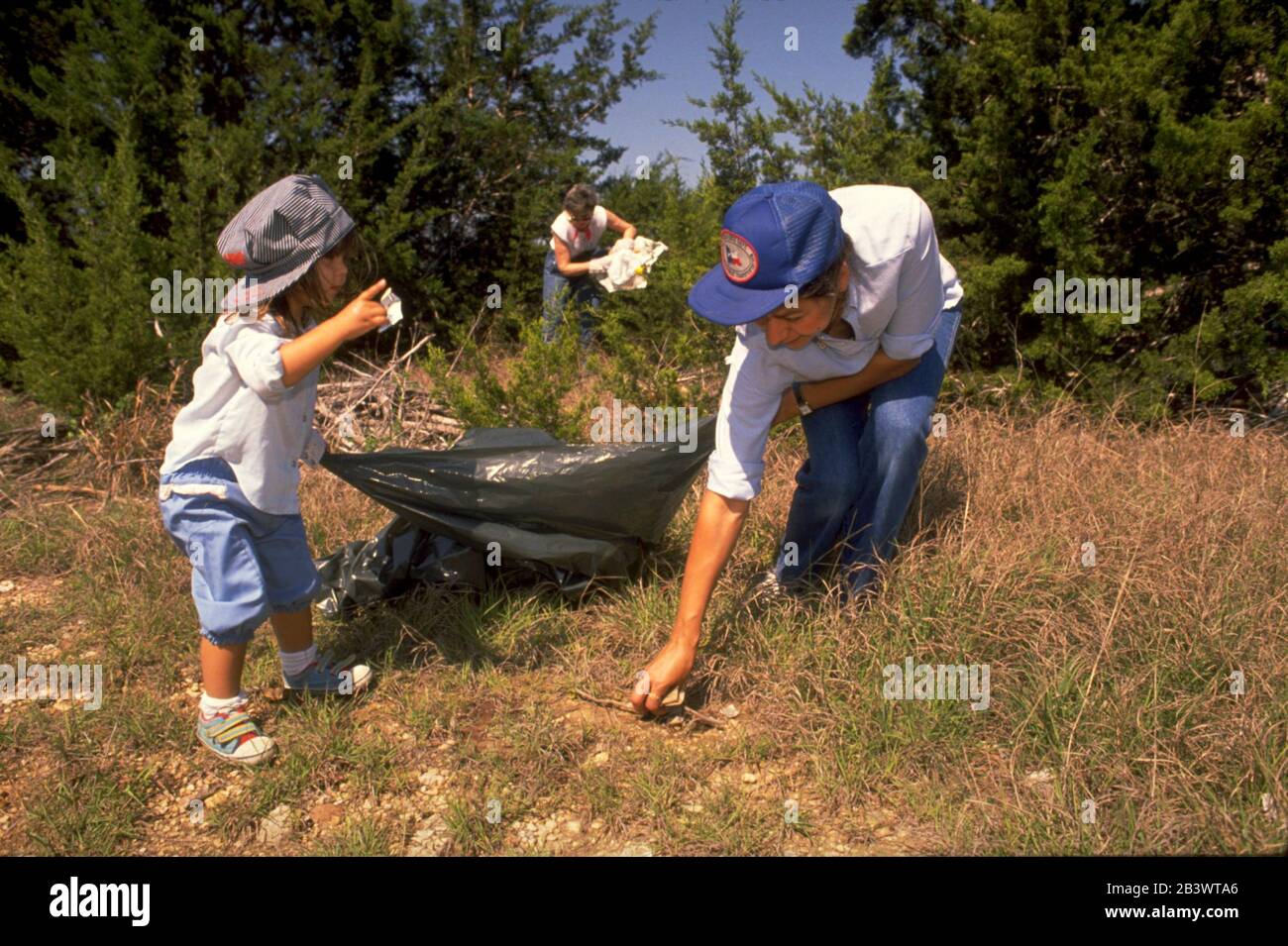Austin Texas USA: La ragazza pre-scuola aiuta i suoi genitori a raccogliere rifiuti sulla proprietà della città durante la giornata annuale di pulizia dei parchi. ©Bob Daemmrich Foto Stock