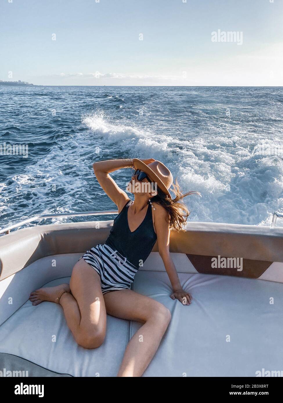 Donna rilassata che gode di un viaggio in oceano, navigando sullo yacht di lusso vicino alla splendida costa rocciosa. Immagine realizzata sul telefono cellulare Foto Stock