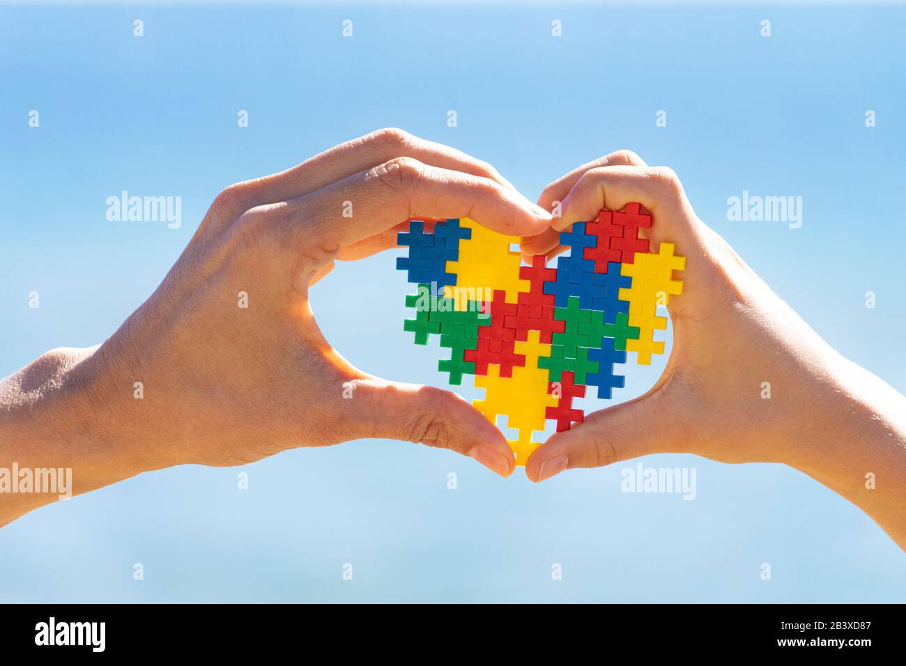 Mani per bambini e adulti che tengono il cuore colorato sullo sfondo blu del cielo. Mondo autismo concetto di giorno di consapevolezza Foto Stock