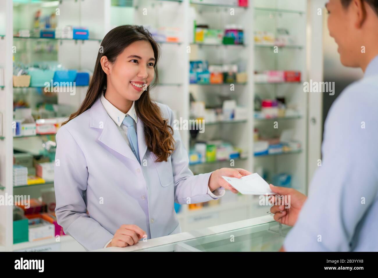 Fiducioso asiatici femmina giovane farmacista con un bel sorriso amichevole e di ricevere il farmaco prescrizione da uomo paziente in farmacia farmacia. Med Foto Stock