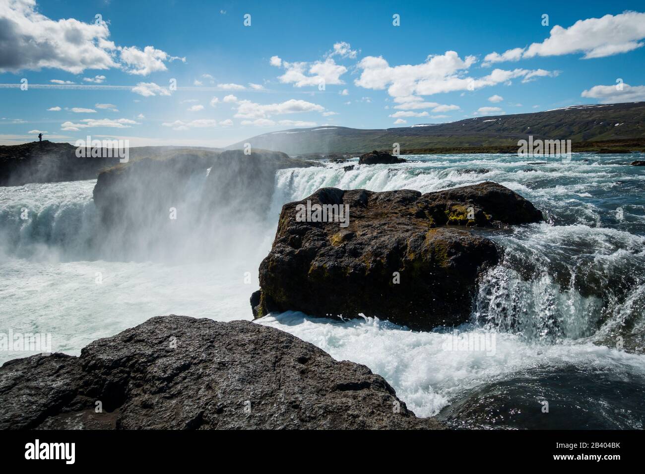 Possente cascata Godafoss vicino Akureyri Islanda nella bella giornata di sole con nebbia sospesa in aria. Cielo blu con alcune nuvole. Silhouette di singola persona in piedi in distanza. Foto Stock