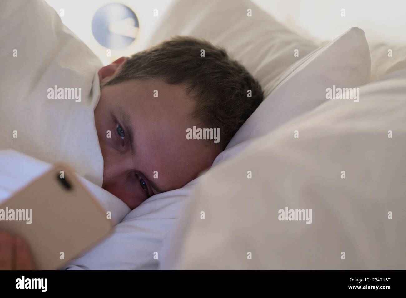 Ritratto di giovane stanco sonno maschio sdraiato a letto sotto la coperta utilizzando smartphone a tarda notte, non può dormire. Insonnia, nomofobia, disturbi del sonno Foto Stock