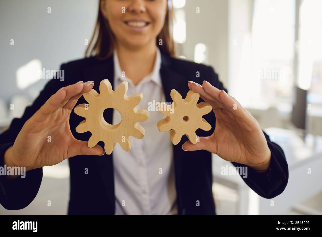 Businesswoman senza volto che tiene gli ingranaggi di legno nelle sue mani nell'ufficio con le finestre Foto Stock