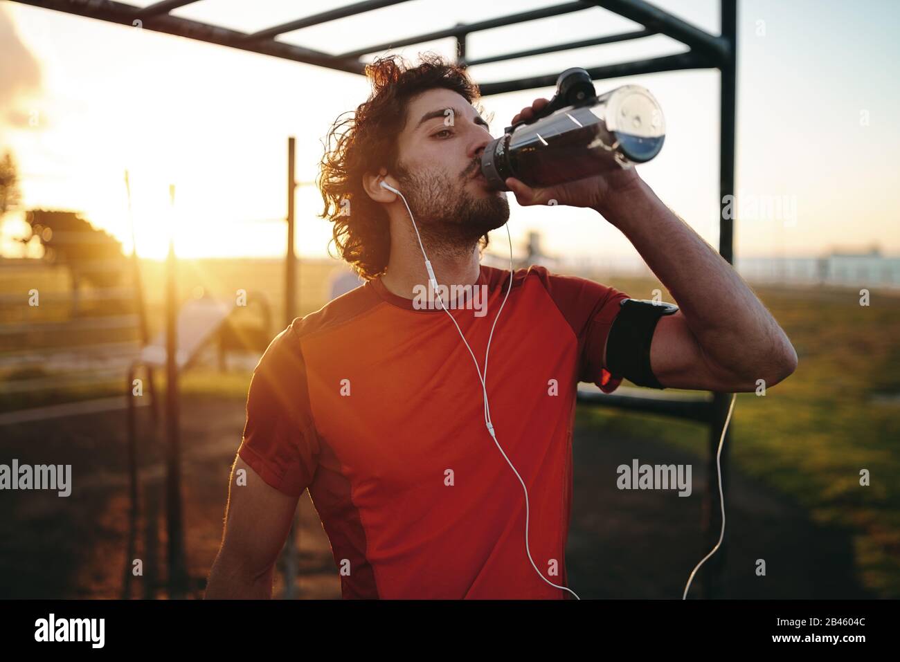 Primo piano ritratto di un giovane caucasico con auricolari nelle sue orecchie bere acqua dopo l'esercizio nel parco all'aperto palestra Foto Stock