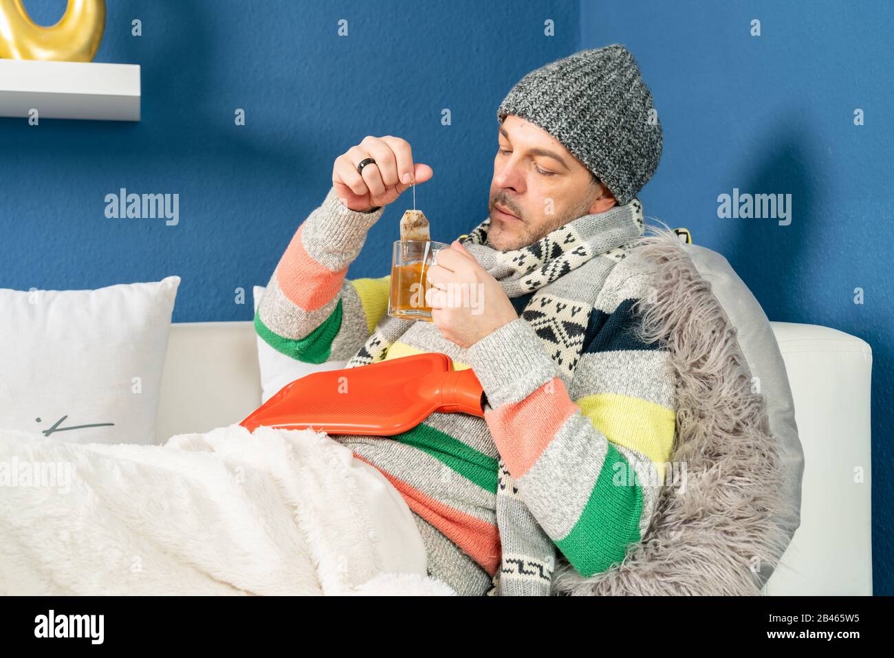 un uomo con un freddo si trova sul divano e bevande tè Foto Stock