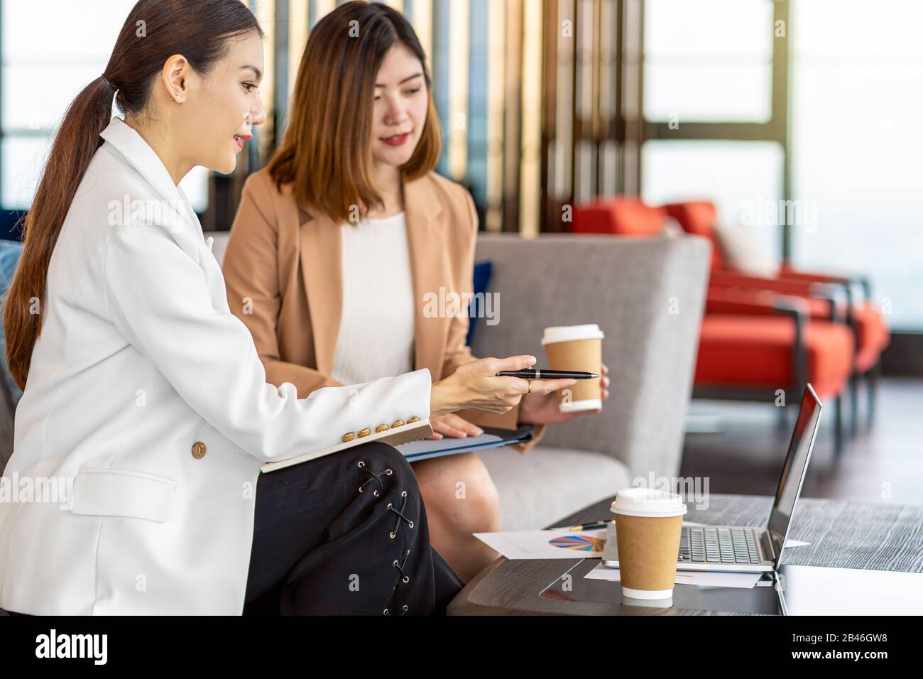Due donne d'affari asiatiche che lavorano con il commercio del socio dalla penna del punto al laptop di tecnologia nell'ufficio moderno o nello spazio di coworking, pausa del caffè, partn Foto Stock