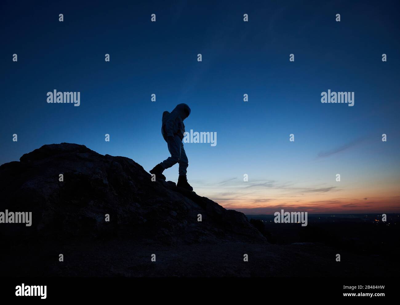 Silhouette di viaggiatore spazio su montagna rocciosa con maestoso cielo notturno sullo sfondo. Cosmonaut in tuta spaziale esplorare nuovo pianeta. Concetto di viaggio spaziale e bellezza crepuscolo. Foto Stock