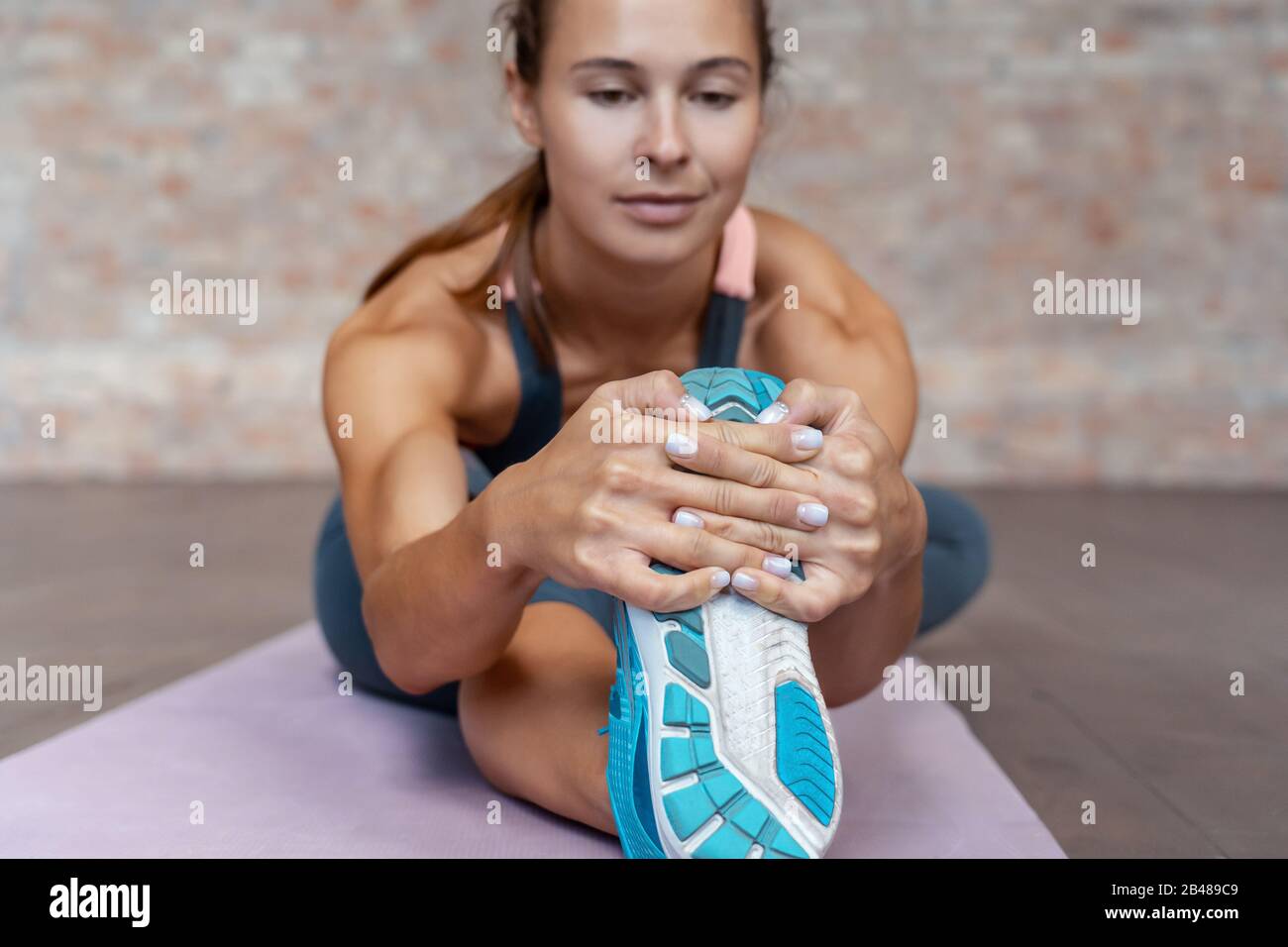 Sportivo giovane donna allenatore fitness riscaldare gamba elasticizzata sul tappeto. Foto Stock