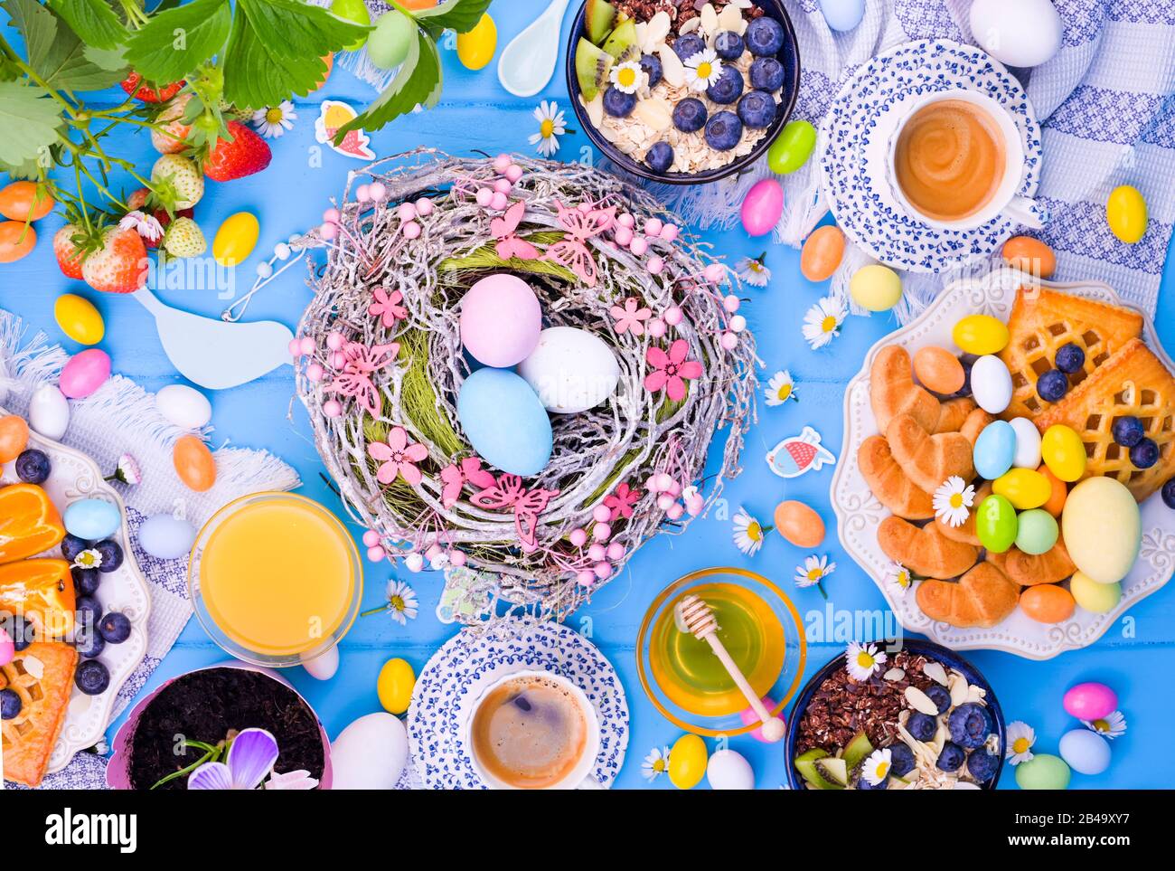 Colazione di Pasqua piatto lay. Caffè espresso, torta con marmellata, biscotti, succo d'arancia fresco, frutta, granola, miele, fragole con foglie e frutti di bosco sul tavolo. Uova colorate per la Domenica di Pasqua. Foto Stock