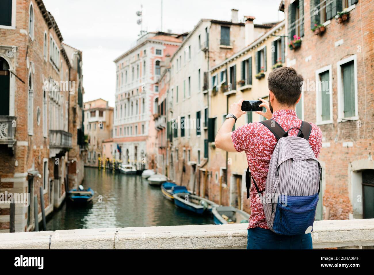 Giovane viaggiatore scattando una foto con il suo smartphone di un canale a Venezia, Italia Foto Stock