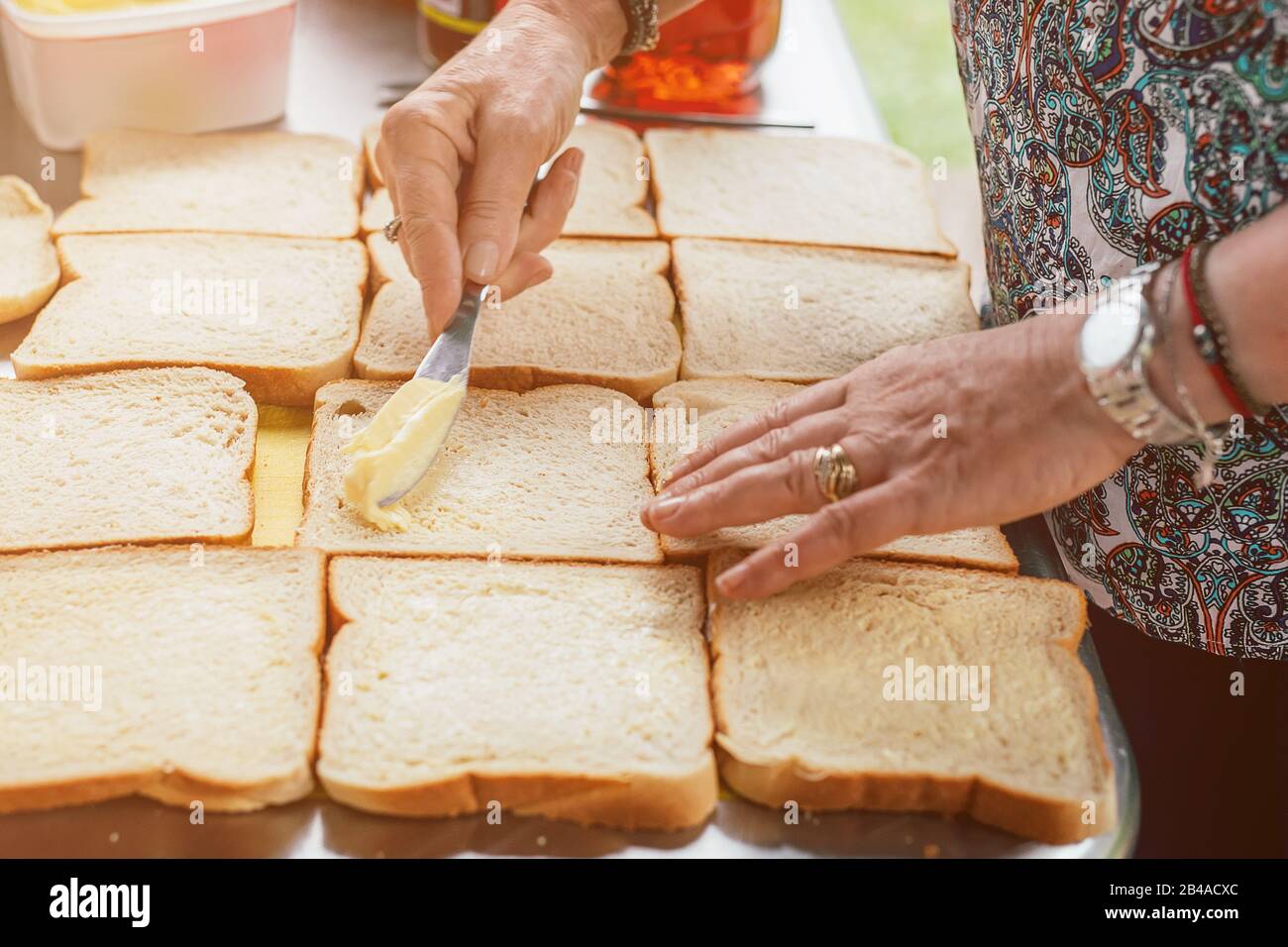Donna anziana che spalma saporito pane bianco con burro a tavola. Preparare il cibo per molte persone. Foto Stock