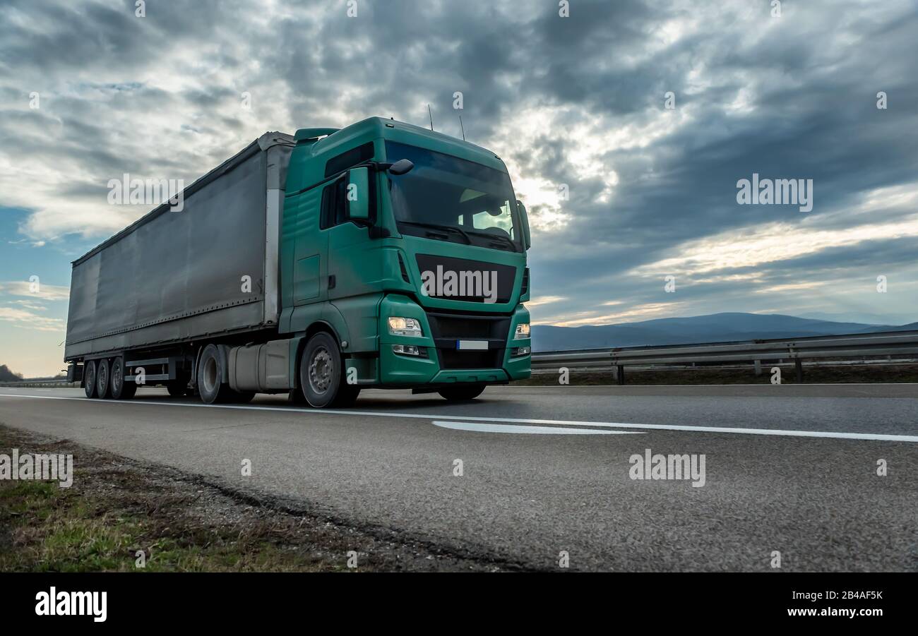 Camion semi-rimorchio verde che guida su un'autostrada con cielo spettacolare tramonto sullo sfondo. Veicolo di trasporto Foto Stock
