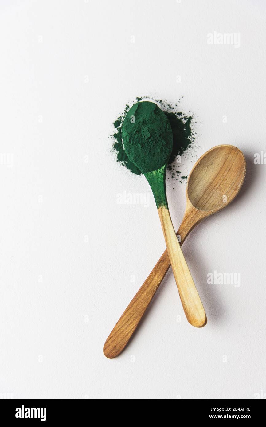 Cucchiai di legno con polvere di spirulina, superfood su fondo bianco, verticale, cucchiaio pieno Foto Stock