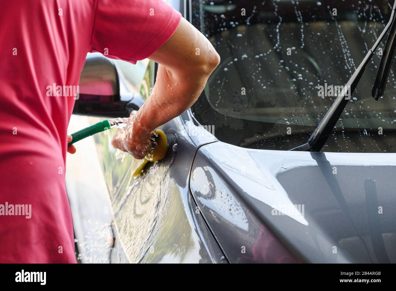Uomo lavoratore lavaggio e sfregamento auto con spugna e acqua Foto Stock