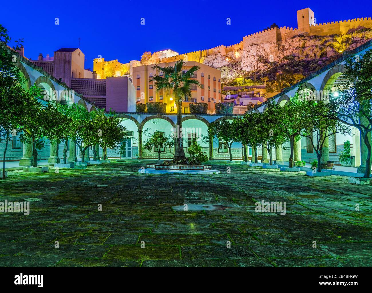 Patio de Los Naranjos nell'ora blu, con l'Alcazaba, illuminato sullo sfondo, città di Almeria, Andalusia, Spagna Foto Stock