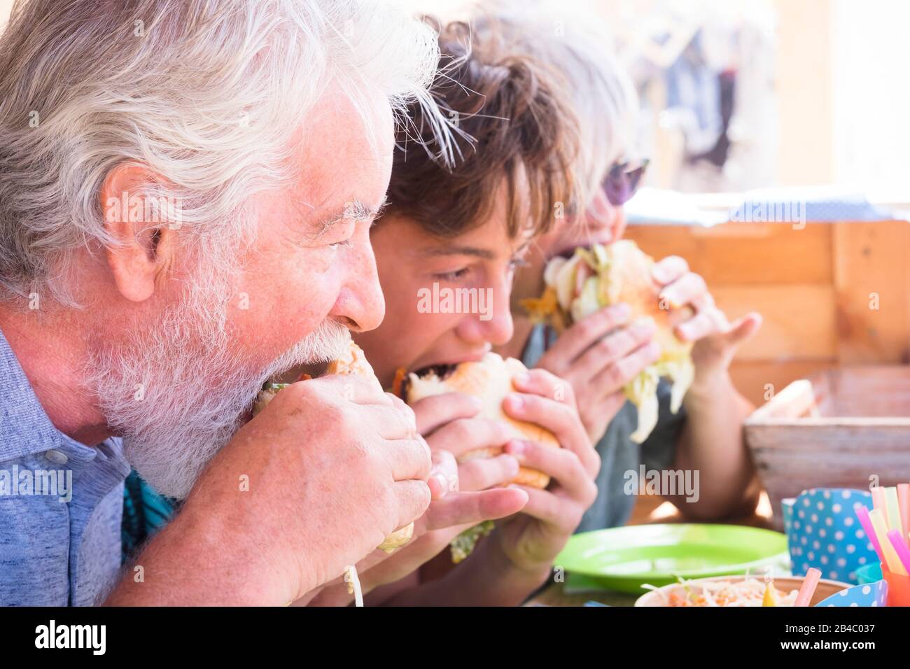 Anziani e giovani adolescenti che mangiano hamburger tutti insieme - nonni con il concetto di amicizia nipote - caucasico bello adulto e giovane mangiare a casa o fast food Foto Stock