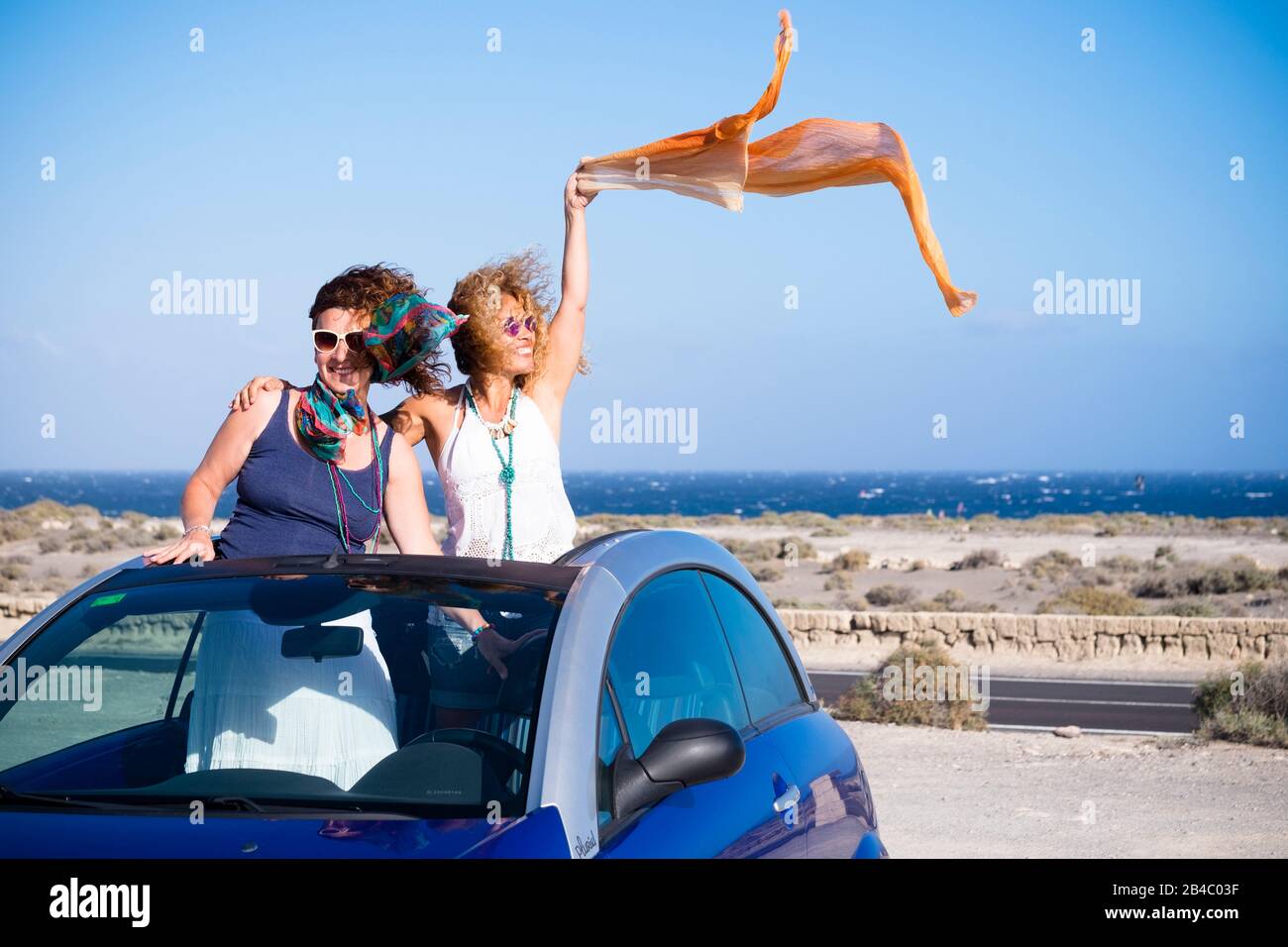 Felice gente libera in vacanza di viaggio - coppia di amici caucasici donne godere dello stile di vita di vacanza estivo stare fuori di una macchina convertibile insieme divertirsi e sorridere - sfondo oceano Foto Stock