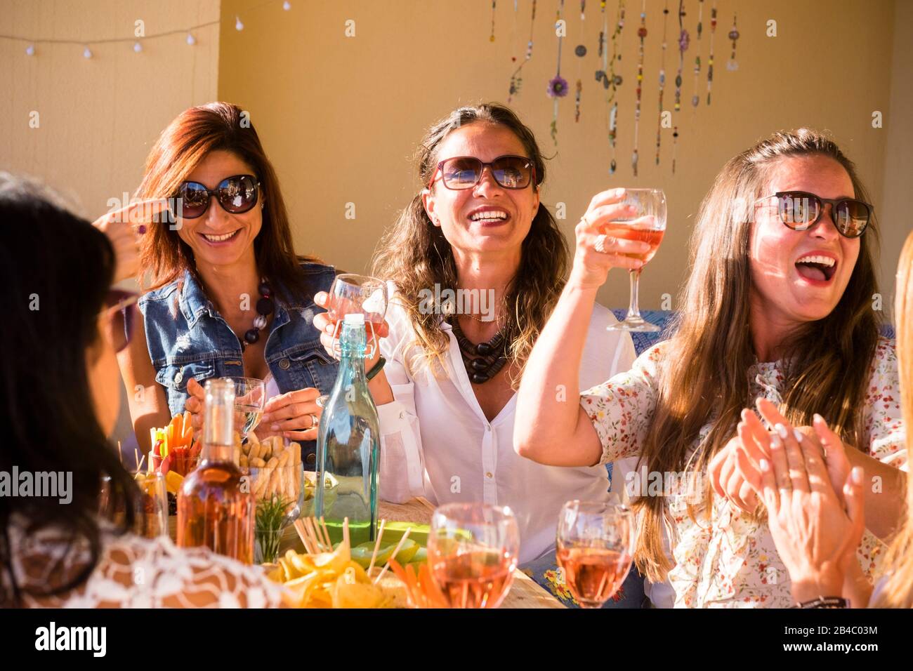 Gruppo di persone caucasiche donne amici celebrare insieme con tavola piena di cibo e tostatura con vino rosso - felicità e amicizia per adulti e giovani donne al ristorante o a casa Foto Stock
