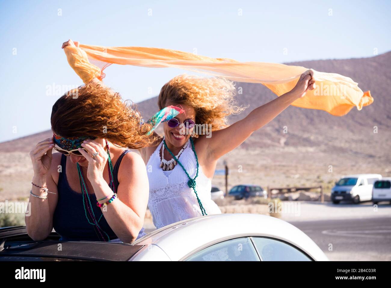 Felice coppia di bella libera indipendente gente allegro donne all'aperto da una auto convertibile giocare con il vento in un concetto di viaggio di guida per vacanze estive Foto Stock