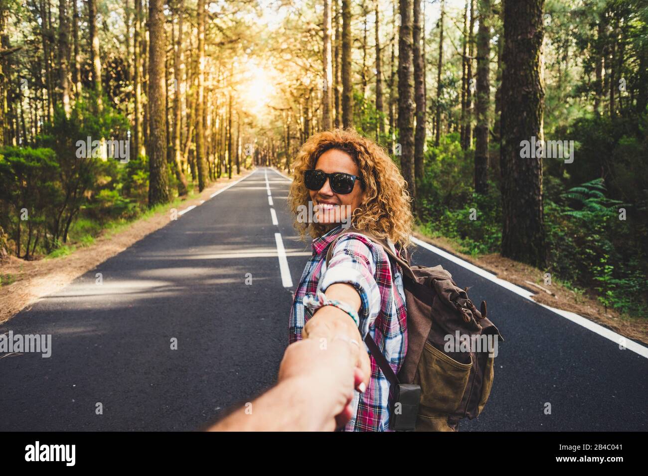 Coppie viaggiatori uomo e donna seguono le mani di tenuta a lungo strada foresta paesaggio e sole sullo sfondo Amore e Viaggi emozioni felici stile di vita concetto. Persone che viaggiano avventure attive vacanze Foto Stock