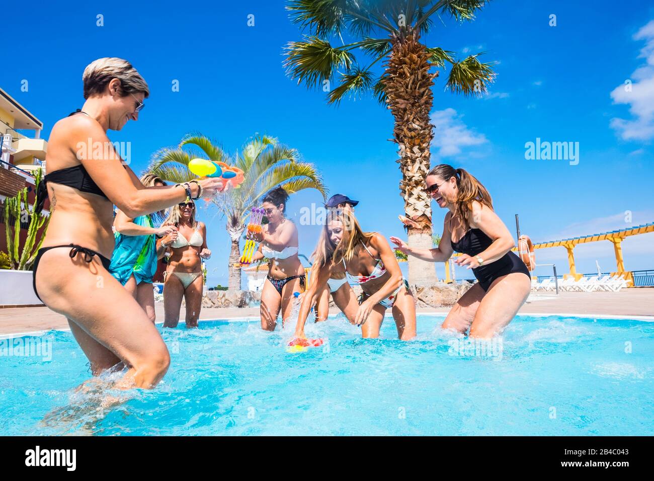 Gioiosa e amicizia con il gruppo di donne che si divertono giocando con le pistole ad acqua in piscina - concetto di vacanza estiva presso il resort - stile di vita di viaggio per una bella mezza età Foto Stock