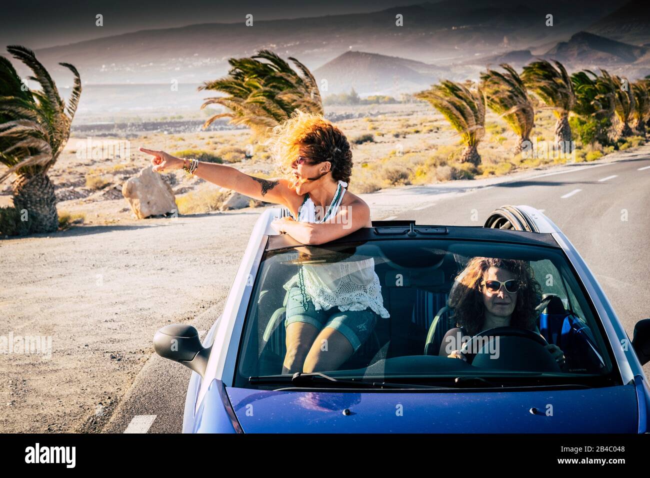 Felicità e viaggi lifestyle persone - coppia di donne adulti amici guidare e viaggiare su un auto blu convertibile - fuori dal tetto piuttosto curly bionda femmina guardando e godendo il viaggio Foto Stock