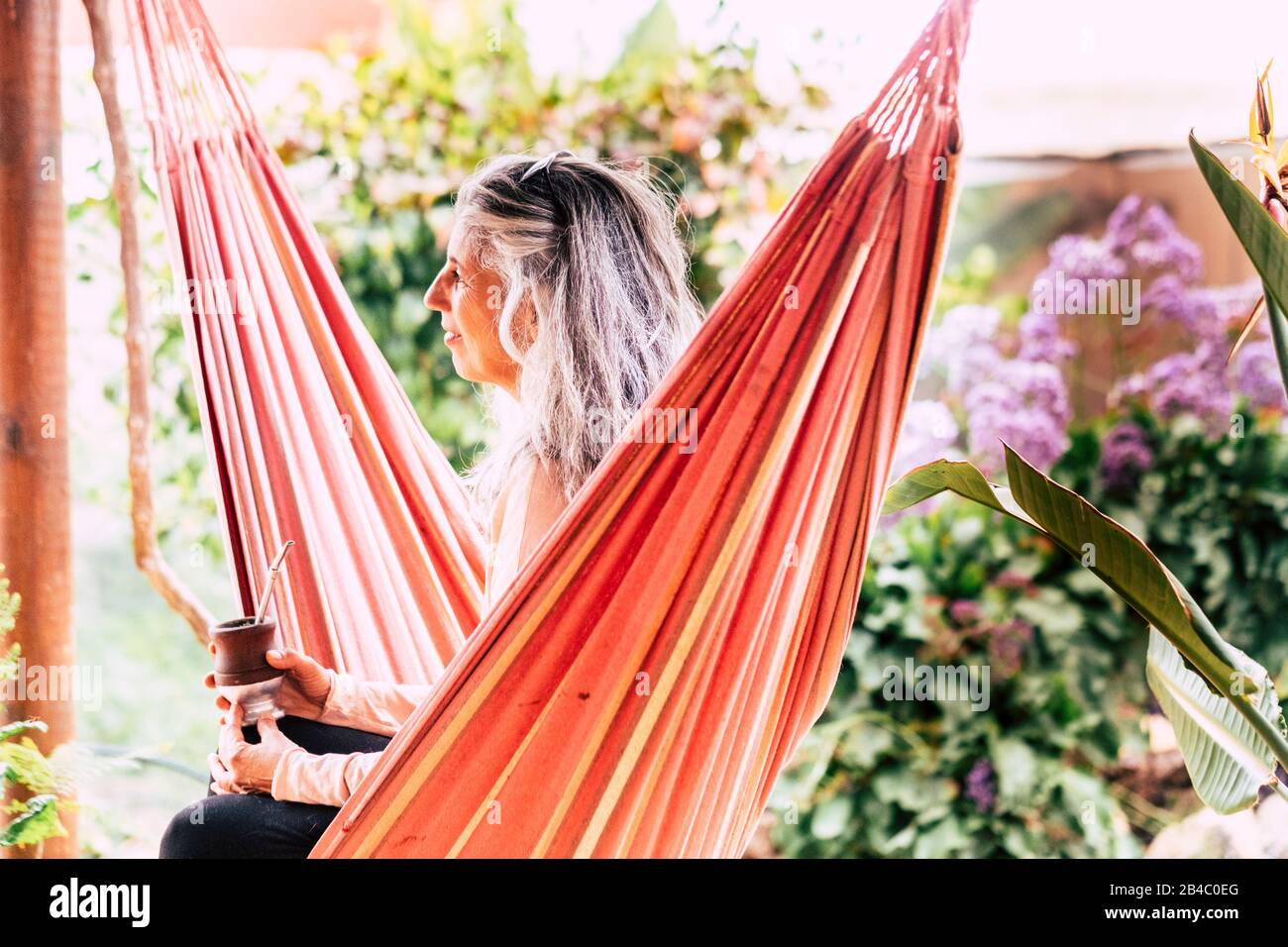 Bella bianca capelli caucasica signora seduta su amaca colorata bere tè e godere l'attività all'aperto relax tempo libero - godendo della natura e stile di vita Foto Stock