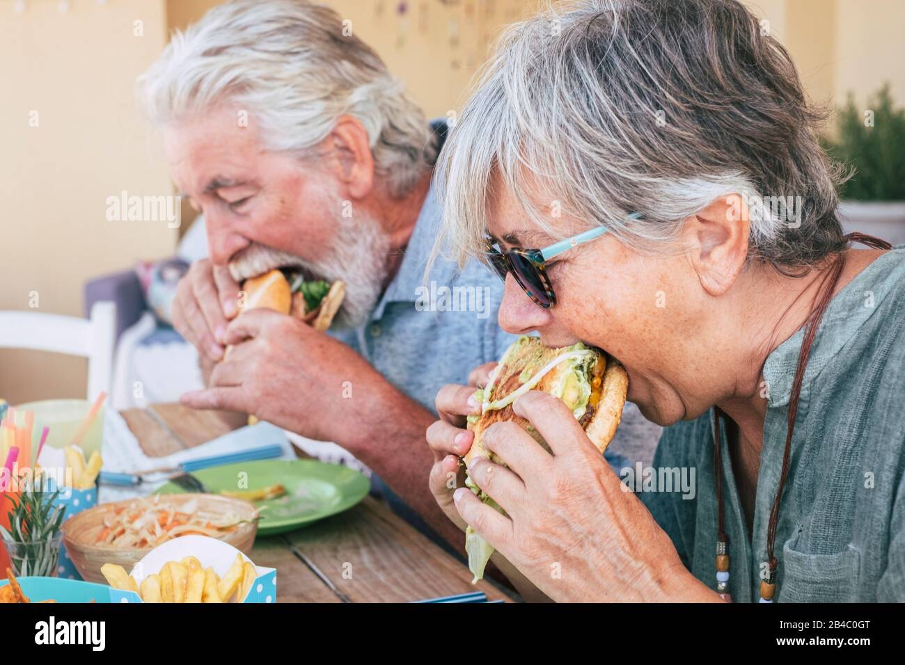 Le persone che mangiano cibo spazzatura hamburger - Un Paio di uomini anziani e donne con fast food pranzo tempo - primo piano di anziani senza uno stile di vita sano - gustoso panino pieno di tutto Foto Stock