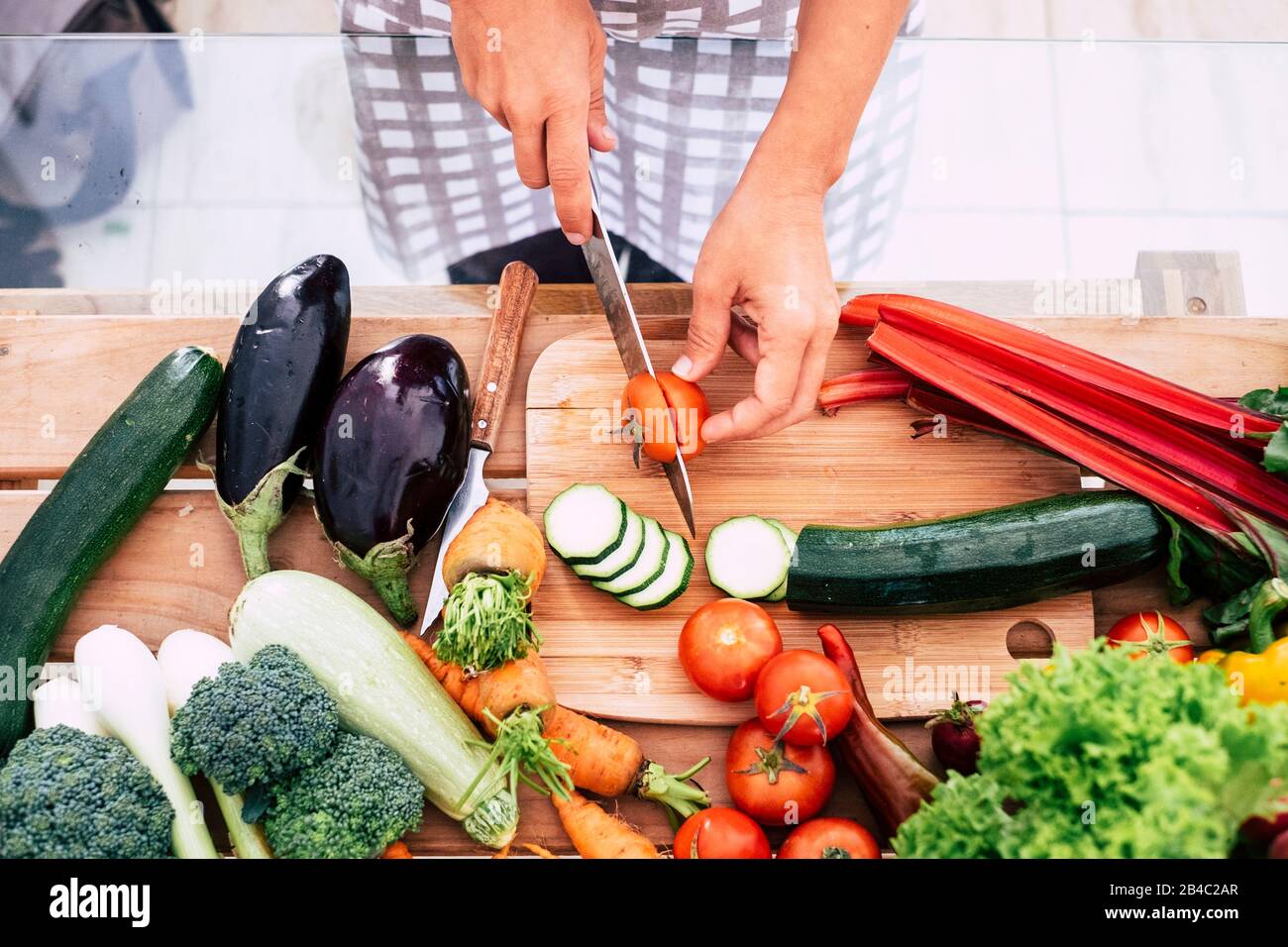 primo piano di tavola piena di verdure come pomodori, carote e più - adulto o senior tagliare cibo in cucina a casa o ristorante - vegano e vegetariano stile di vita e dieta Foto Stock