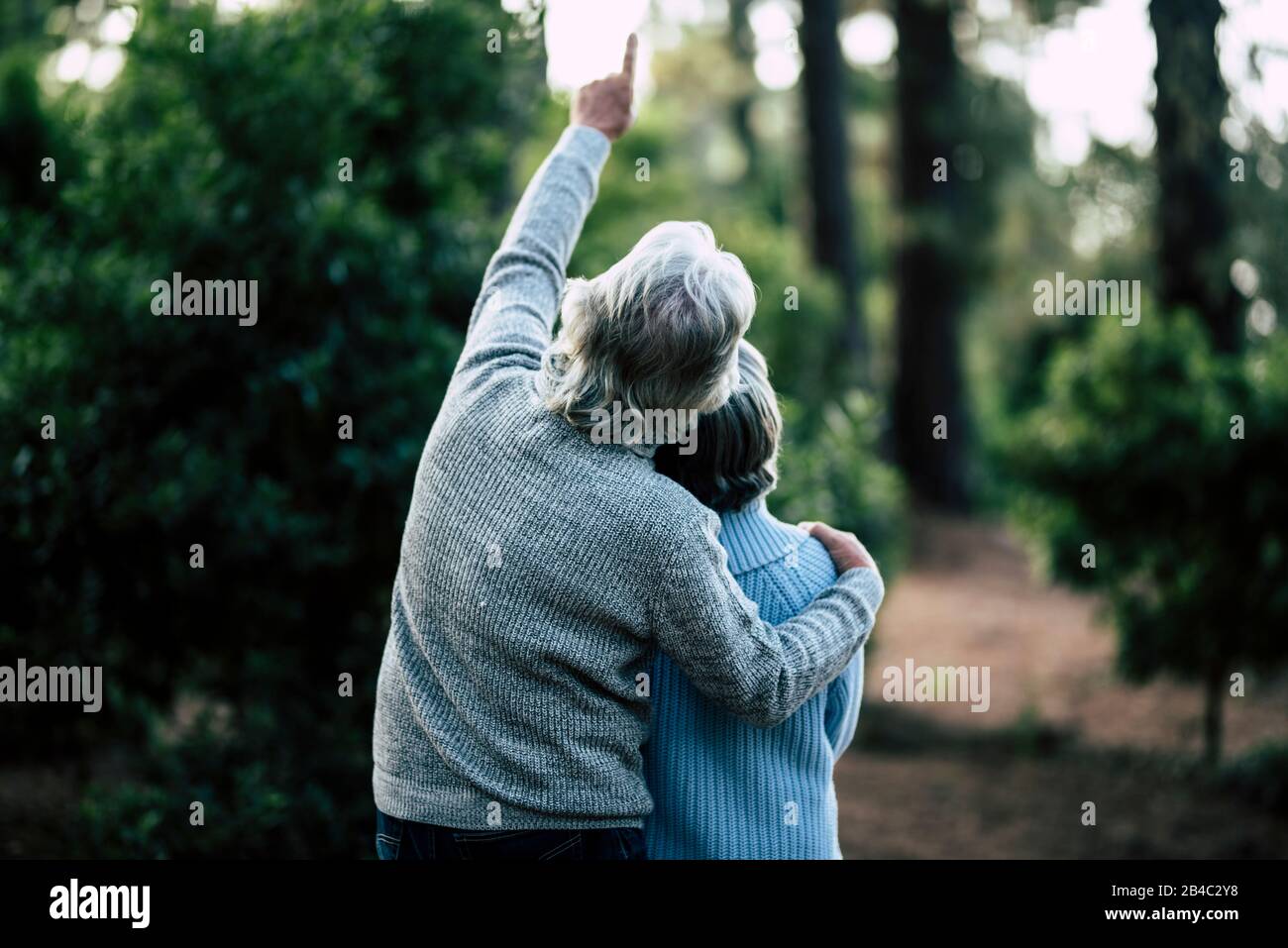 Coppia di anziani maturi abbracciano e godono l'attività di svago all'aperto insieme nella foresta - alberi verdi sullo sfondo - uomo irriconoscibile e donna per anziani sano ilstile Foto Stock