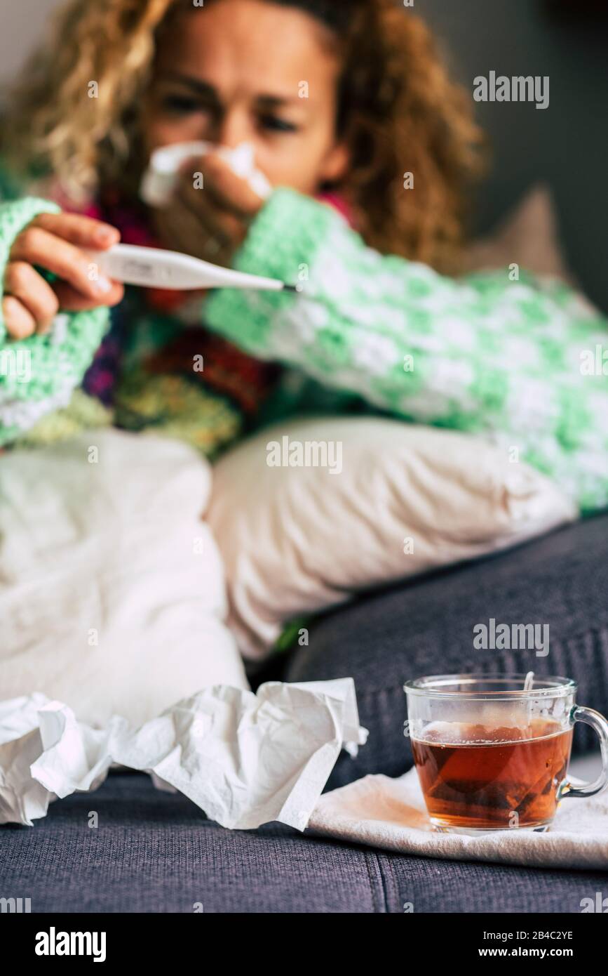 Concetto di malattia fredda stagionale con donna adulta che controlla la febbre e beve tè di hoth ealthy a casa che si posa sul divano - popolo caucasico in inverno con problemi sani Foto Stock