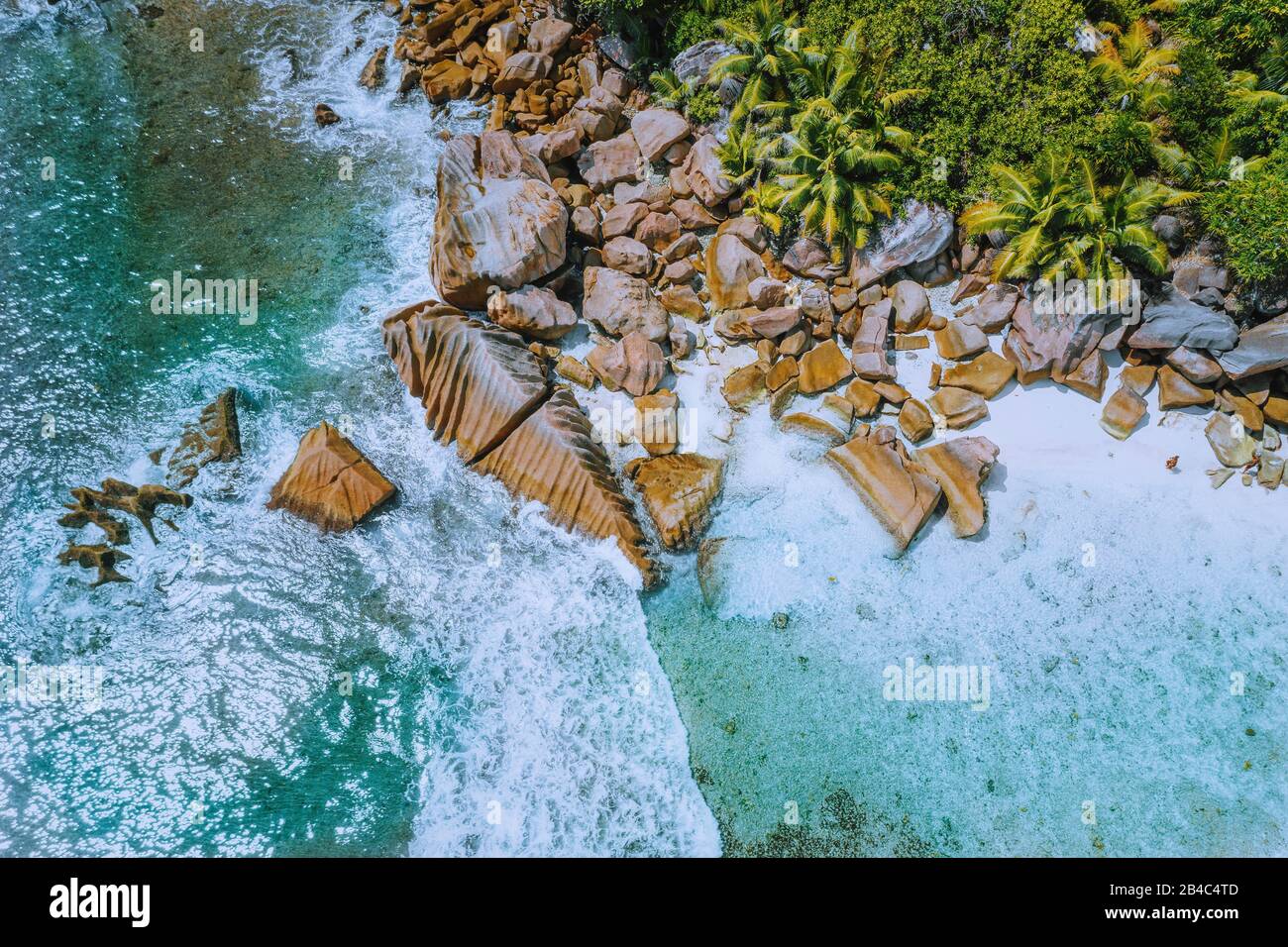 Anse Cocos spiaggia isola tropicale la Digue Seychelles. Vista aerea del drone delle onde oceaniche in schiuma che rotolano verso la costa rocciosa e le palme. Foto Stock