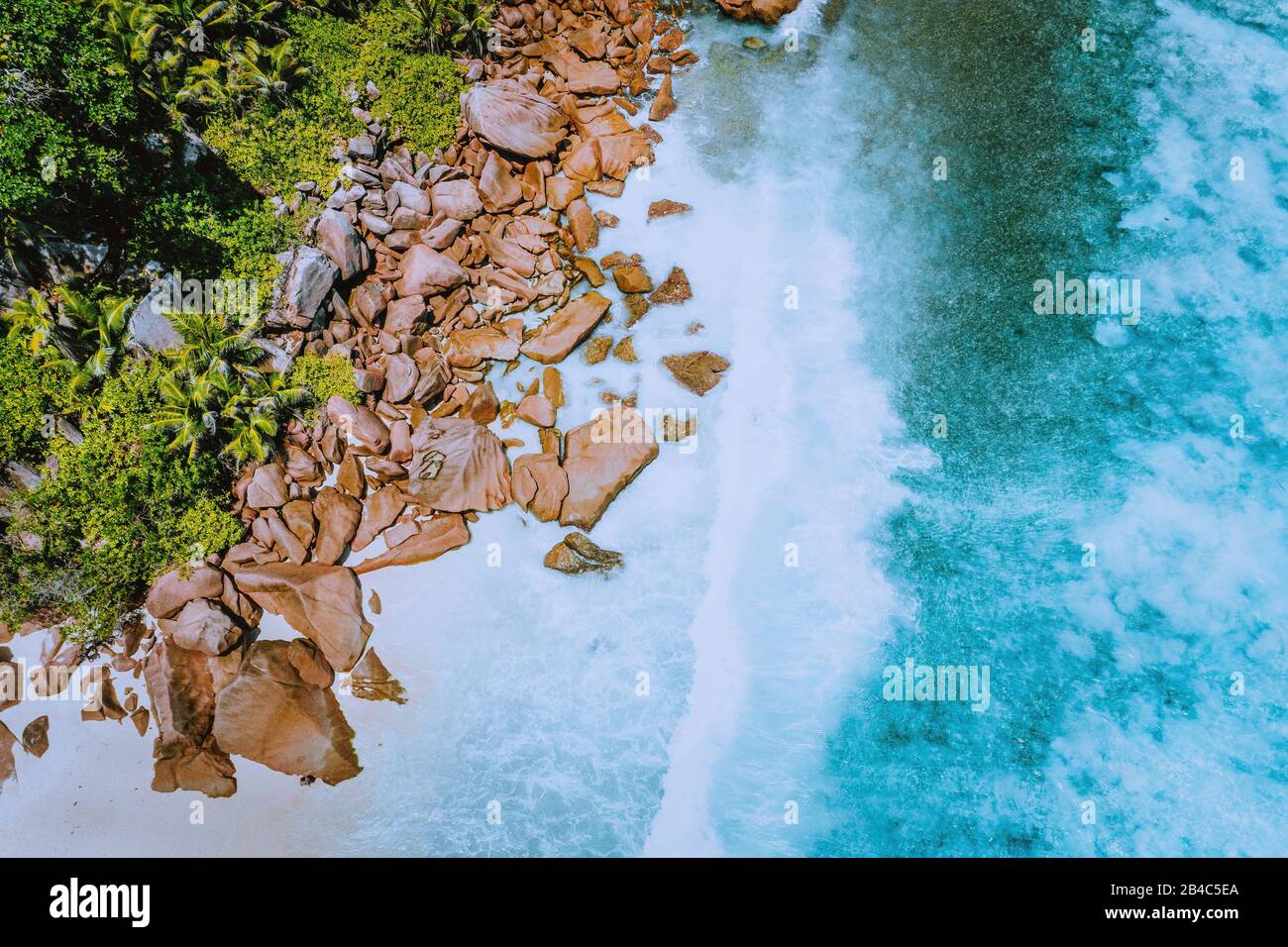 Seychelles Isola Di La Digue. Veduta aerea delle onde dell'oceano che colpiscono enormi rocce di granito bizzarre sulla spiaggia tropicale anse Cocos con acque azzurre turchesi. Incredibile scogliera di roccia marina nella costa. Foto Stock