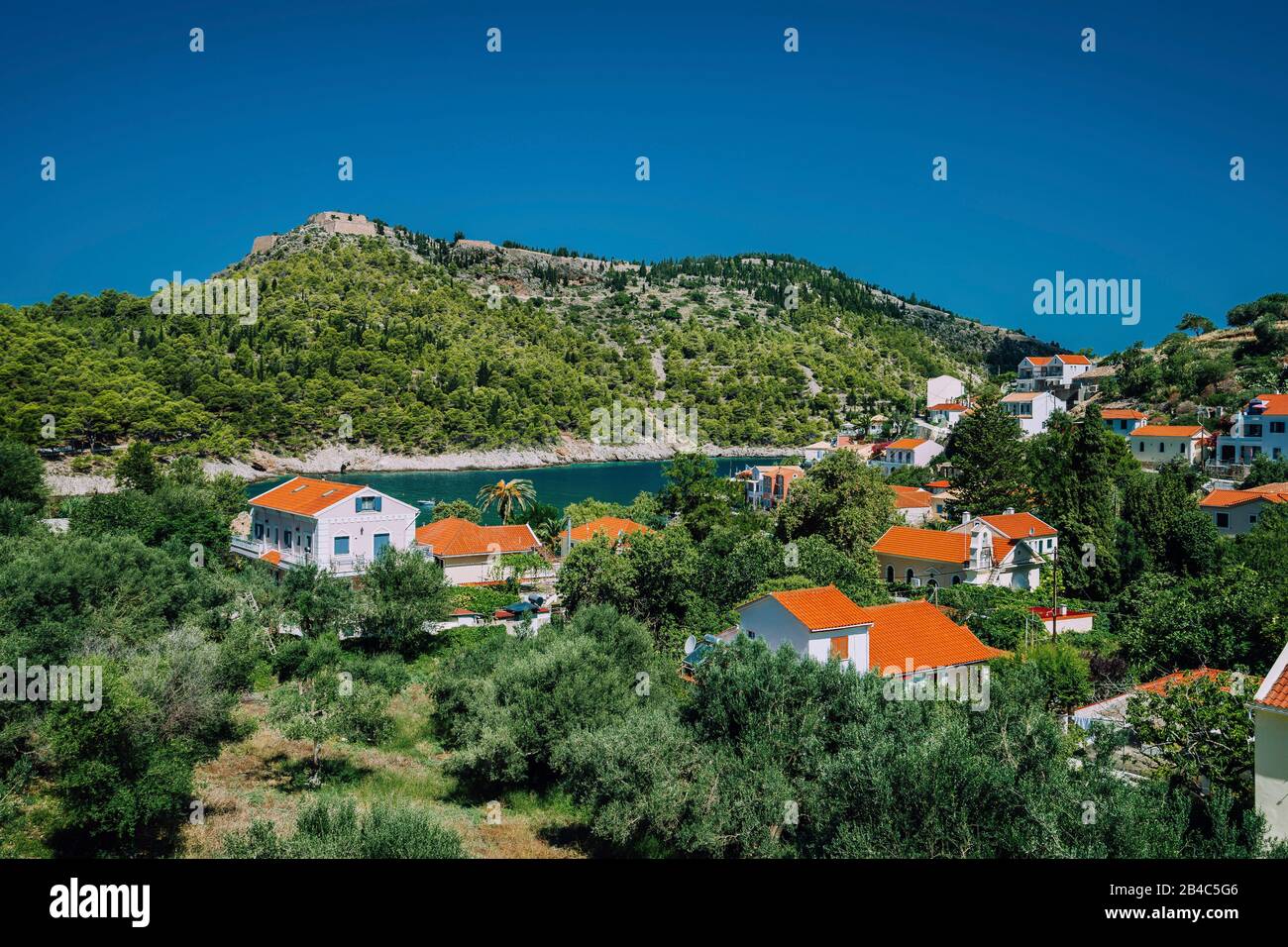 Città accogliente, rilassante sensazione di estate. Tetti rossi di Assos villaggio alla lussureggiante verde Mediterraneo luogo dell'isola di Kefalonia. Foto Stock