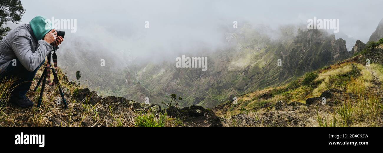 Scatto panoramico del viaggiatore facendo foto di incredibile terreno montuoso ripido con la lussureggiante valle del canyon sul percorso dalla Valle di Xo-Xo. Macchina Fotografica Su Treppiede.Isola Di Santo Antao, Capo Verde. Foto Stock