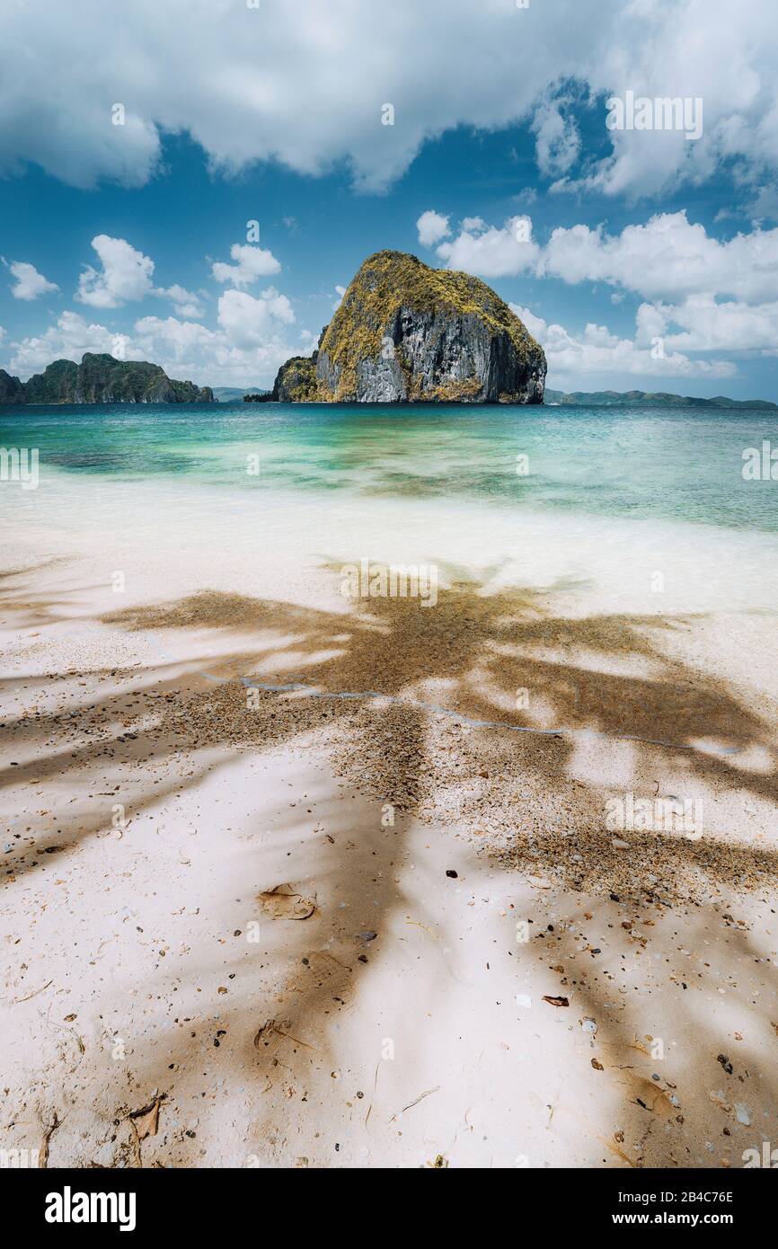 Palme ombre sulla spiaggia tropicale di Las Cabanas con incredibile e unica isola di Pinagbuyutan sullo sfondo. Bellissimo paesaggio a El Nido, Palawan, Filippine. Foto Stock