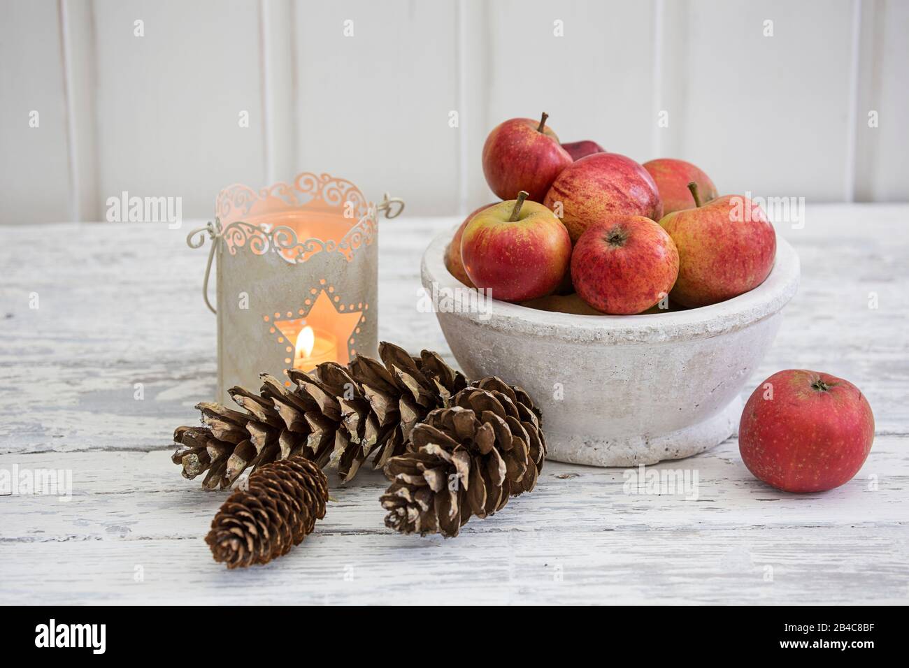 ancora vita con mele rosse, candela e coni di pino in stile scandinavo su legno bianco Foto Stock