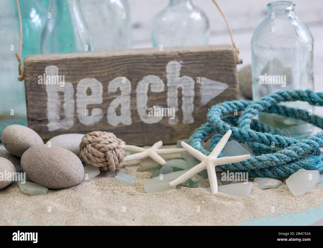 Ancora vita nautica con segno di spiaggia in legno, corda, ghiaia e vecchie bottiglie blu Foto Stock