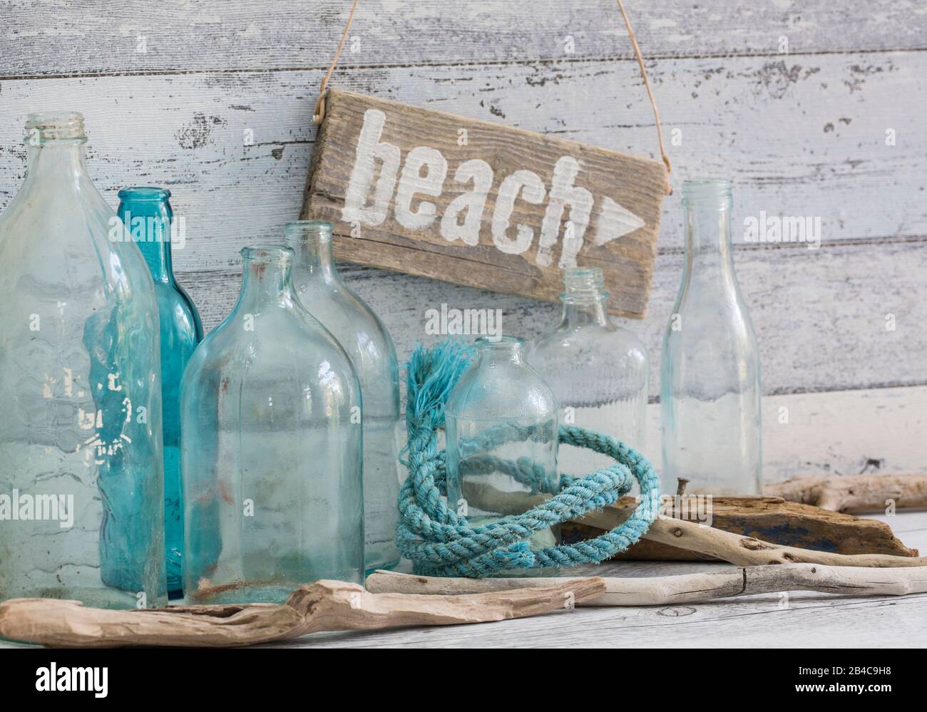 Ancora vita nautica con segno di spiaggia in legno, corda e vecchie bottiglie blu Foto Stock