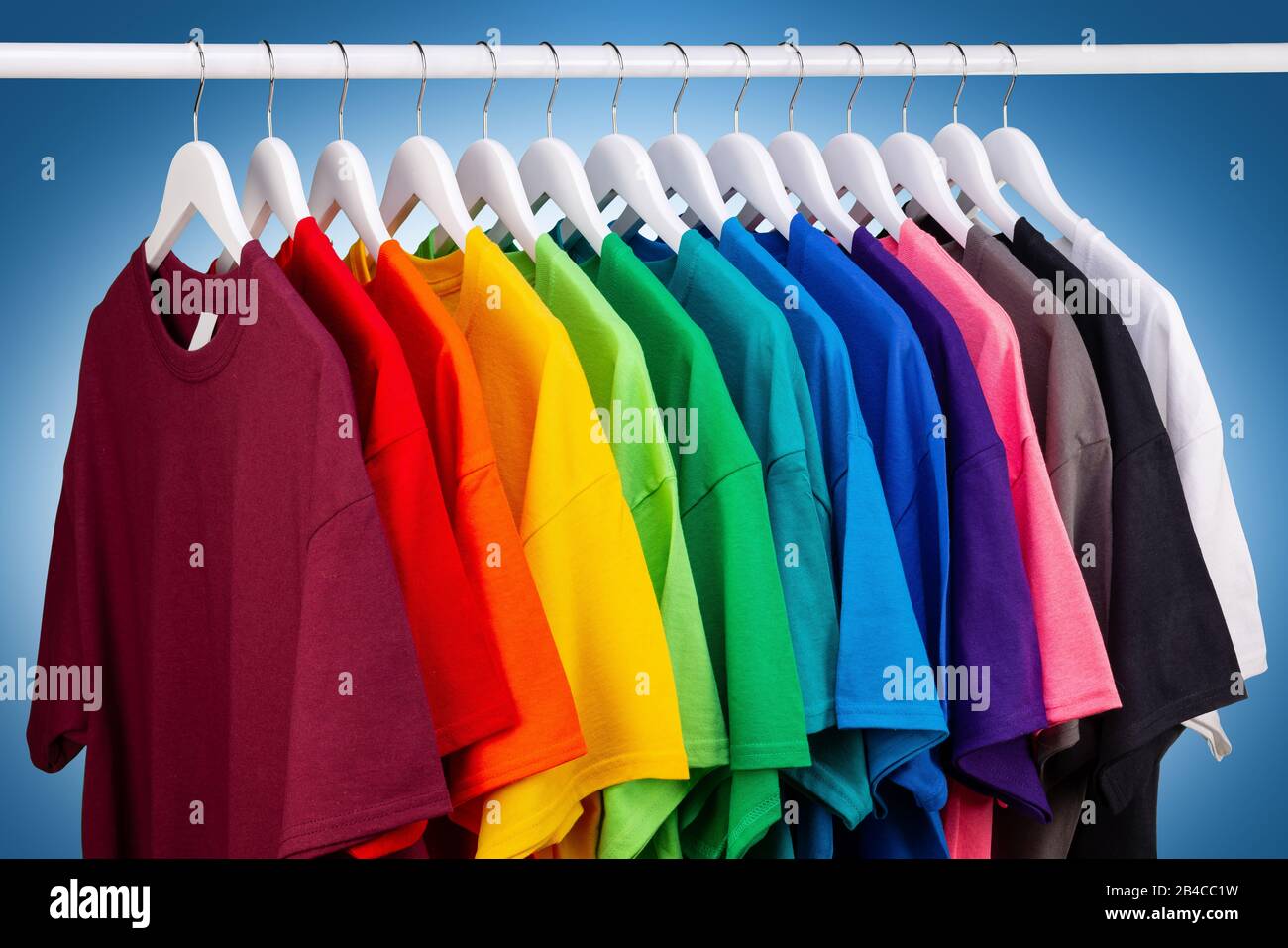 fila di nuove magliette in cotone fresco in colori arcobaleno colorati che si impiccano sul binario dei vestiti in strdrobe. Varie camicie colorate su dorso bianco blu Foto Stock