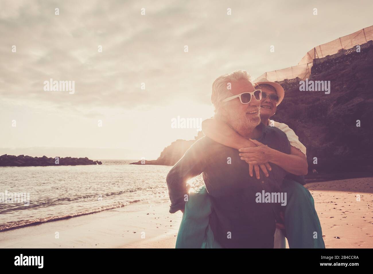 bella coppia di anziani in spiaggia divertirsi insieme e giocare - uomo maturo portare la moglie donna con amore e per sempre concetto di vita - mare o oceano in background - vacanza stile di vita in pensione Foto Stock