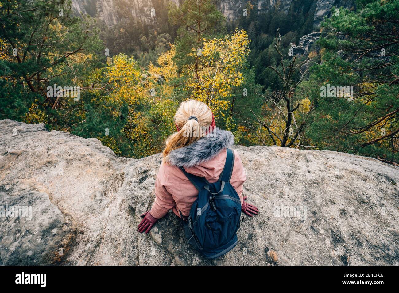 Biondo Frau in winterlicher Kleidung mit zaino, sitzt am Rand einer Felsklippe, Reise-Lifestyle-Konzept Foto Stock