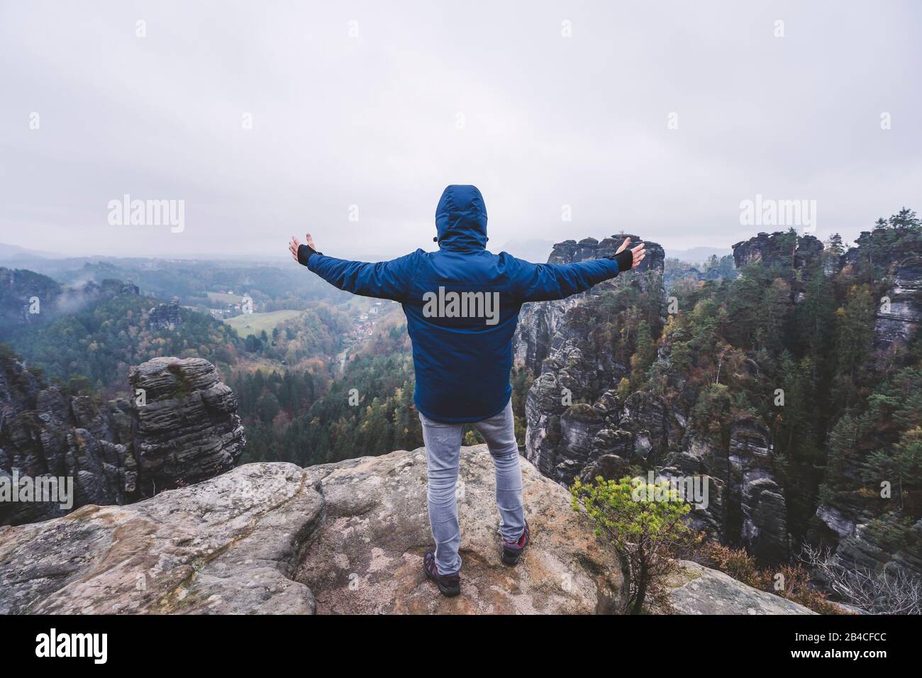 Wanderer steht auf dem Gipfel eines Berges, genießt die Aussicht über Berge und Wälder im tal, Reise-Lifestyle-Abenteuer-Konzept Foto Stock