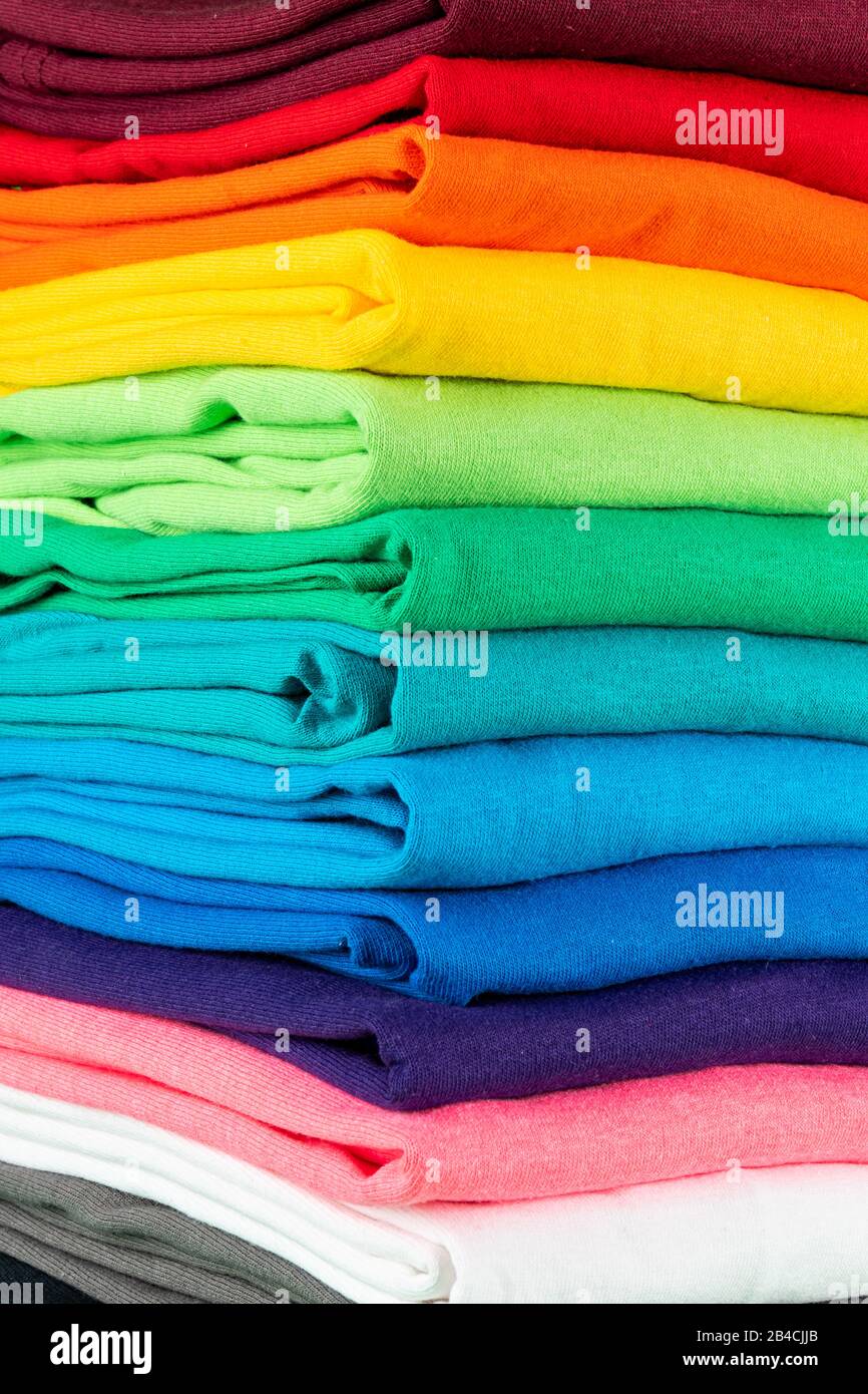 primo piano di molte nuove magliette in cotone in tessuto fresco in colori arcobaleno colorati. Pile di varie camicie colorate di sfondo Foto Stock