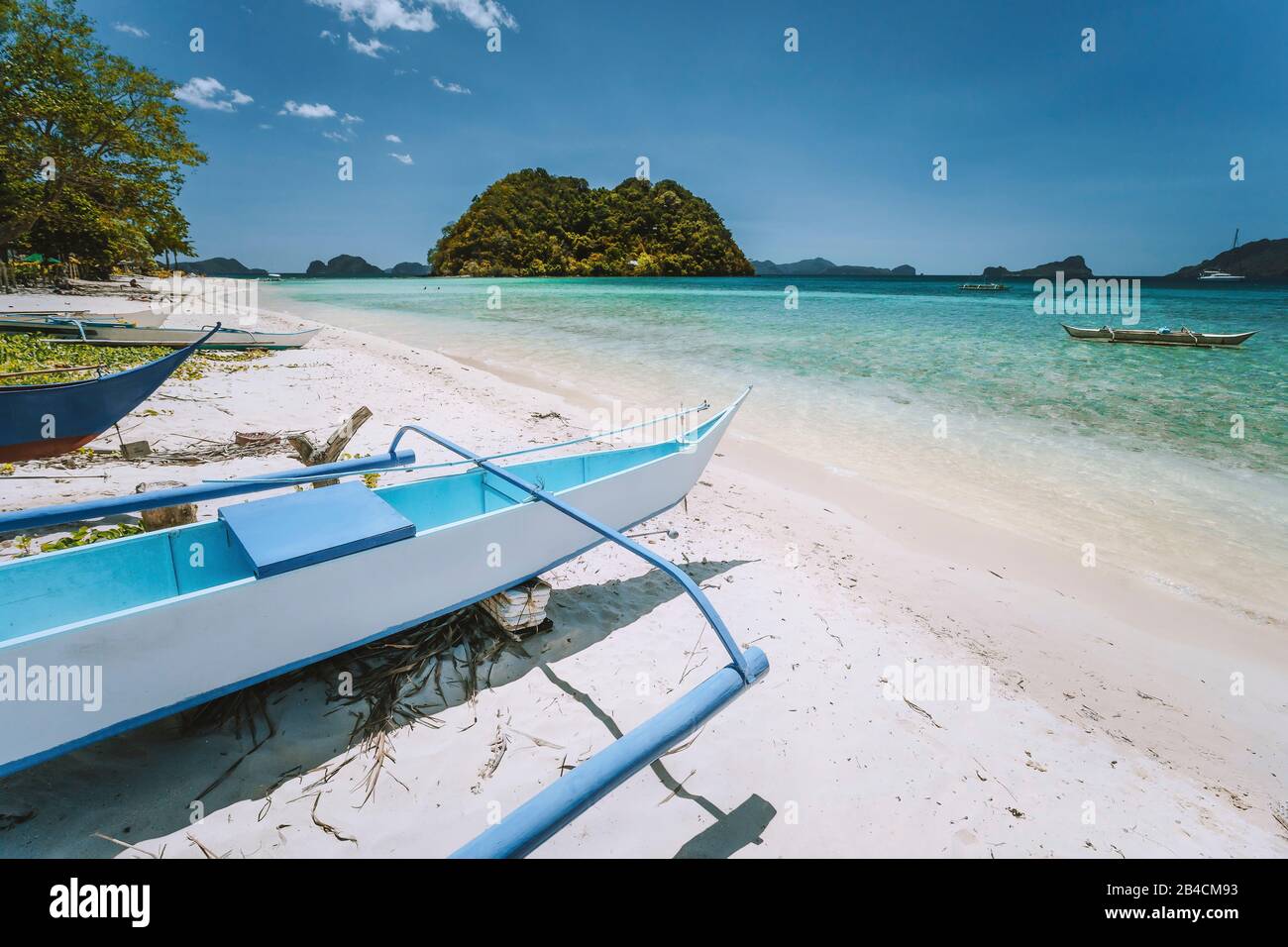 El Nido, Palawan, Filippine. Barca bianca banca sulla spiaggia di Las Cabanas con isola tropicale sullo sfondo. Bellissimo paesaggio. Foto Stock